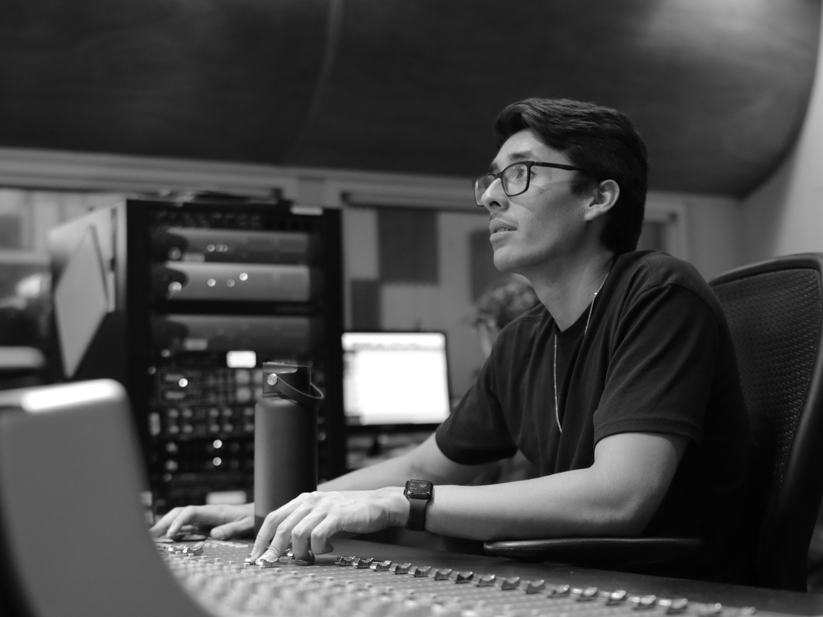 A black and white photo of Mateo Baxley mixing a song, his hands moving a slider on the mixing board